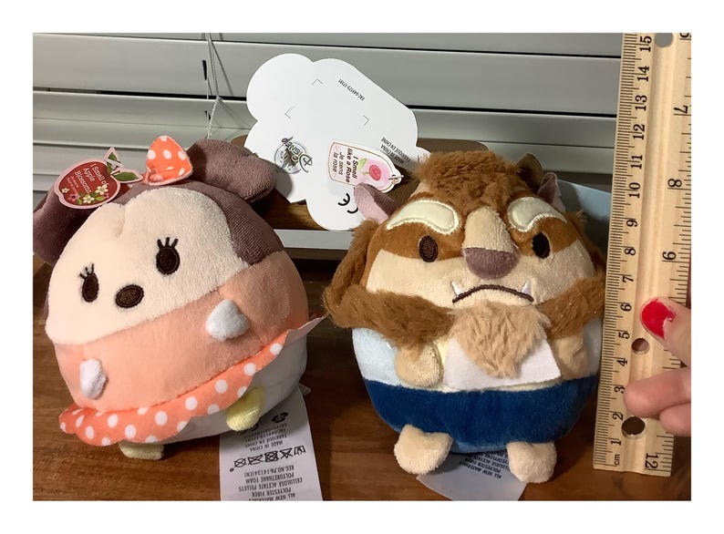 May include: Two plush character toys. One is a light pink and white character with a polka dot bow. The other is a brown and tan character with a blue outfit. A ruler shows the toys are approximately 4 inches tall.
