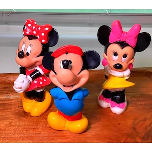 Pu&ograve; includere: Tre statuette vintage di Topolino e Minnie. Topolino indossa una camicia blu, pantaloncini rossi e un cappello rosso. Minnie indossa un vestito rosso a pois bianchi e un fiocco rosso. L'altra Minnie indossa un vestito giallo e un fiocco rosa.