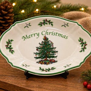 May include: White oval serving platter with a green scalloped edge and the words "Merry Christmas" in green. The platter features a detailed Christmas tree illustration in the center, with holly accents.