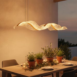 Può includere: Una lunga lampada a sospensione orizzontale con un paralume ondulato in rete bianca traslucida e dettagli color oro. La luce è sospesa tramite fili sottili ed emette un bagliore caldo e soffuso, illuminando lo spazio con una luce diffusa.