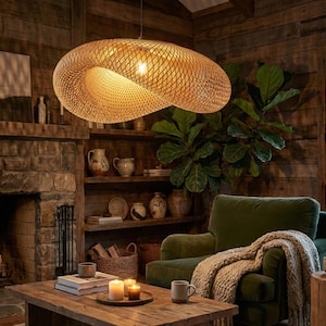 May include: A woven, spiral-shaped pendant light fitting hangs from the ceiling. The light is made of a natural, light brown material and illuminates a cosy living room with a green armchair, wooden coffee table, and a stone fireplace.