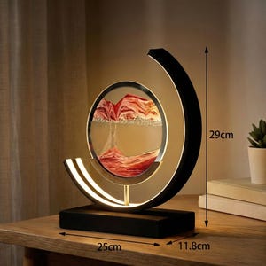 K&ouml;nnte beinhalten: Dekorative Sandkunst-Lampe mit schwarzem Sockel und halbmondf&ouml;rmigem Rahmen. Die Lampe verf&uuml;gt &uuml;ber ein kreisf&ouml;rmiges Glasgeh&auml;use mit rotem und wei&szlig;em Sand, das 29 cm hoch, 25 cm breit und 11,8 cm tief ist.