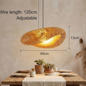 May include: A woven bamboo pendant light, 40cm wide and 13cm high, hangs above a dining table. The wire length is 120cm and adjustable. The light fixture has a warm, natural colour and casts a soft glow. The text on the image says "Wire length: 120cm Adjustable".