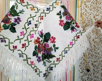 Può includere: Poncho bianco all'uncinetto con un motivo floreale e bordi a frangia. Il design presenta fiori verdi, rosa, viola e blu.