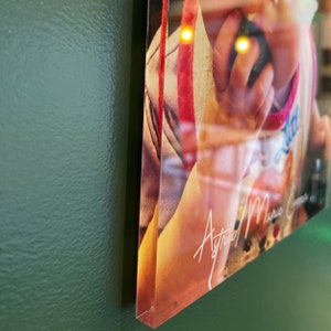 May include: A framed print featuring a child wearing a white and pink shirt with the word "Little" visible. The print has the signature "Astrid Marie Copper" in white script. The frame is visible on the side.