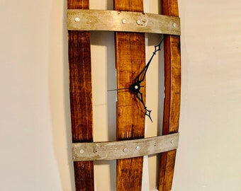 May include: A rustic wall clock made from reclaimed wine barrel staves. The clock face is framed by three wooden slats with metal bands and rivets. The clock hands are black.