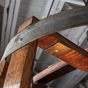 May include: Close-up of a wooden chandelier made from repurposed wine barrels. The chandelier features a circular metal frame and a rustic, distressed finish.