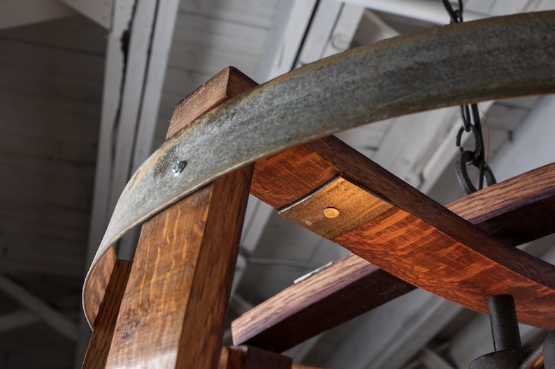 May include: Close-up of a wooden chandelier made from repurposed wine barrels. The chandelier features a circular metal frame and a rustic, distressed finish.