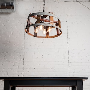 May include: A rustic wooden and metal chandelier with five light bulbs hanging from a white brick wall above a black table.