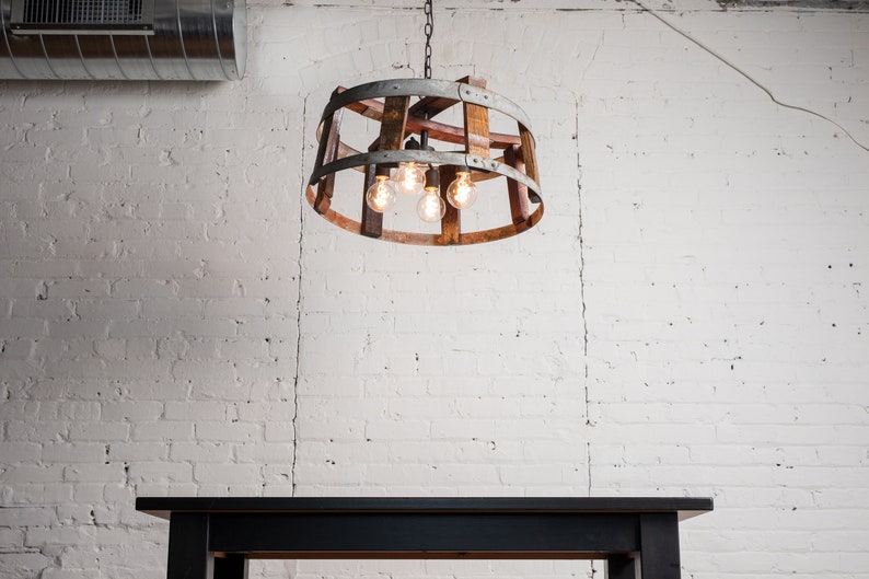 May include: A rustic wooden and metal chandelier with five light bulbs hanging from a white brick wall above a black table.