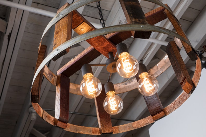 May include: A rustic chandelier made from repurposed wine barrels with five exposed light bulbs. The chandelier is made of wood and metal and has a natural, weathered finish.