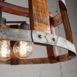 May include: A rustic chandelier made from reclaimed wine barrels with exposed wood and metal accents. The chandelier features three Edison bulb lights.