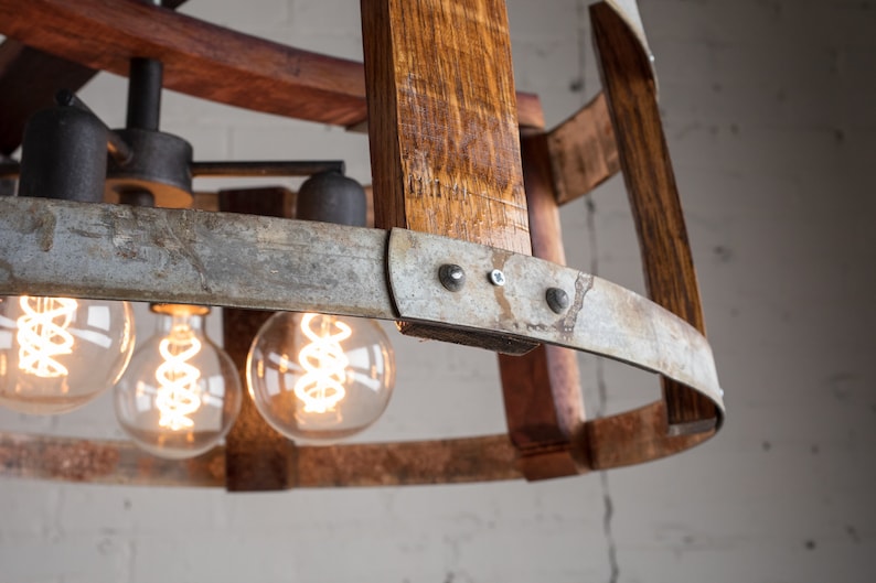 May include: A rustic chandelier made from reclaimed wine barrels with exposed wood and metal accents. The chandelier features three Edison bulb lights.