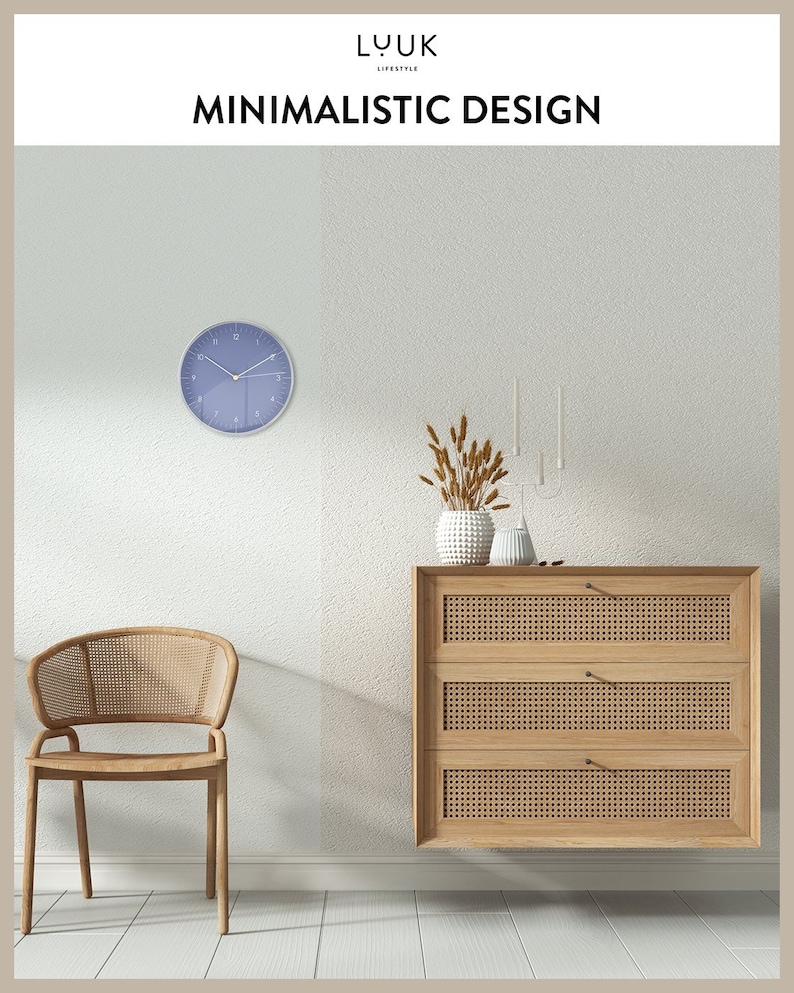 May include: A light blue wall clock with black hands and Roman numerals. The clock is hanging on a white wall. A wooden chair with a woven seat and back is in the foreground. A wooden dresser with three drawers and woven fronts is on the wall. A vase with dried wheat stalks is on top of the dresser.