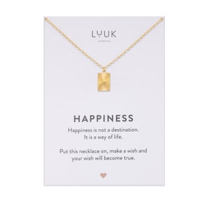Puede incluir: Collar de oro con un colgante cuadrado que dice "Happiness" en una tarjeta blanca. La tarjeta también dice "Happiness is not a destination. It is a way of life. Put this necklace on, make a wish and your wish will become true."