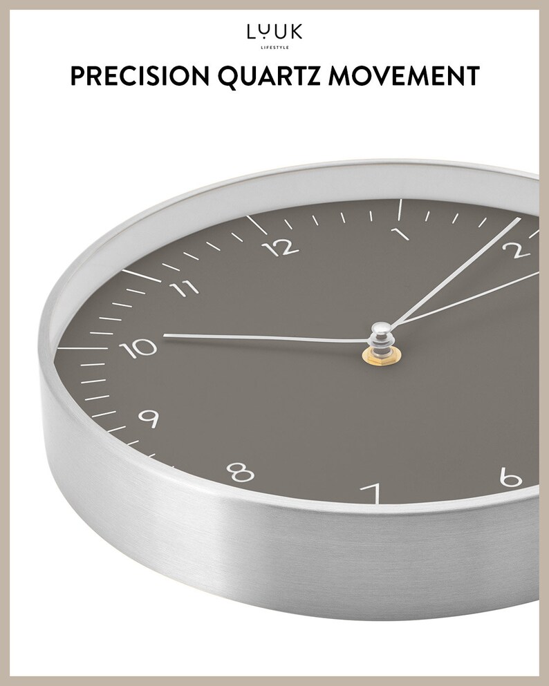 Op de afbeelding: Een close-up van een zilveren en grijze analoge klok met een donkergrijze wijzerplaat en witte markeringen. De wijzers van de klok zijn zilver en de wijzerplaat van de klok geeft "PRECISION QUARTZ MOVEMENT" aan.