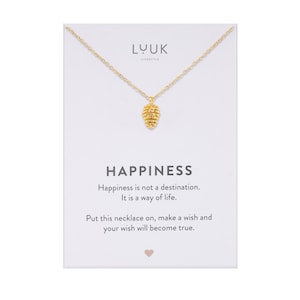 Könnte beinhalten: Goldkette mit einem kleinen Tannenzapfen-Anhänger. Die Karte lautet "Glück ist kein Ziel. Es ist eine Lebensart. Legen Sie diese Kette an, wünschen Sie sich etwas und Ihr Wunsch wird wahr."