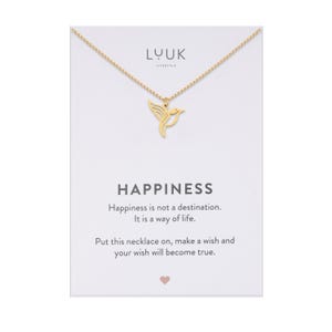 Pode incluir: Colar de ouro com um pingente de beija-flor e um cartão que diz "Felicidade não é um destino. É um modo de vida. Coloque este colar, faça um desejo e seu desejo se tornará realidade."