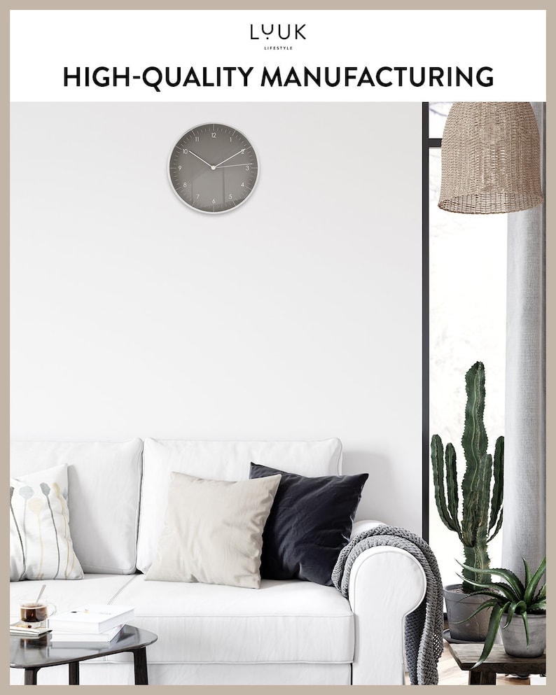 Op de afbeelding: Een witte bank met drie kussens, een grijze deken en een cactusplant in een pot. Boven de bank hangt een grijze klok met witte cijfers. De tekst "LUK LIFESTYLE HIGH-QUALITY MANUFACTURING" staat bovenaan de afbeelding.