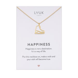 Op de afbeelding: Gouden ketting met een gouden schaats-hanger. De kaart luidt "Geluk is geen bestemming. Het is een manier van leven. Doe deze ketting om, wens iets en je wens zal uitkomen."