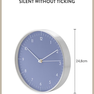 May include: A silver and blue wall clock with white hands and a diameter of 24.8 inches. The clock face is a light blue color with white numbers and a gold center. The clock is silent and does not tick.