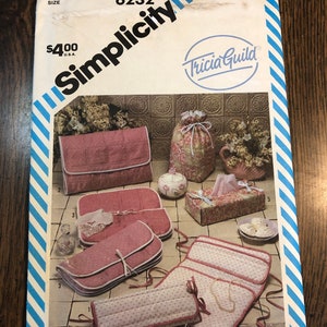 May include: Simplicity sewing pattern number 6232 by Tricia Guild for a set of five pink and white quilted storage bags. The bags are designed for storing jewelry, tissues, and other small items. The pattern includes instructions for making a jewelry roll, a tissue box cover, a small bag, a medium bag, and a large bag.