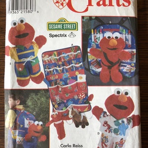 May include: A Simplicity Crafts sewing pattern featuring Sesame Street's Elmo. The pattern includes instructions for making a plush Elmo toy, a backpack, a wall organizer, and a set of clothes. The pattern is for one size.