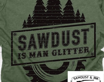 May include: Green t-shirt with a black graphic. The graphic features a saw blade, pine trees, and the text "SAWDUST IS MAN GLITTER". A smaller logo with a rifle and saw is in the lower right corner.