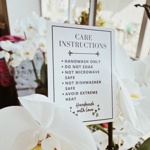 May include: A rectangular white card with a thin black border featuring the text CARE INSTRUCTIONS followed by bullet points: HANDWASH ONLY, DO NOT SOAK, NOT MICROWAVE SAFE, NOT DISHWASHER SAFE, AVOID EXTREME HEAT, and the phrase Handmade with love.