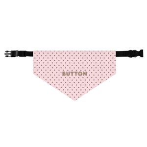 May include: A pink dog bandana with a polka dot pattern and the name "BUTTON" printed in the center. The bandana is attached to a black adjustable collar with a plastic buckle.