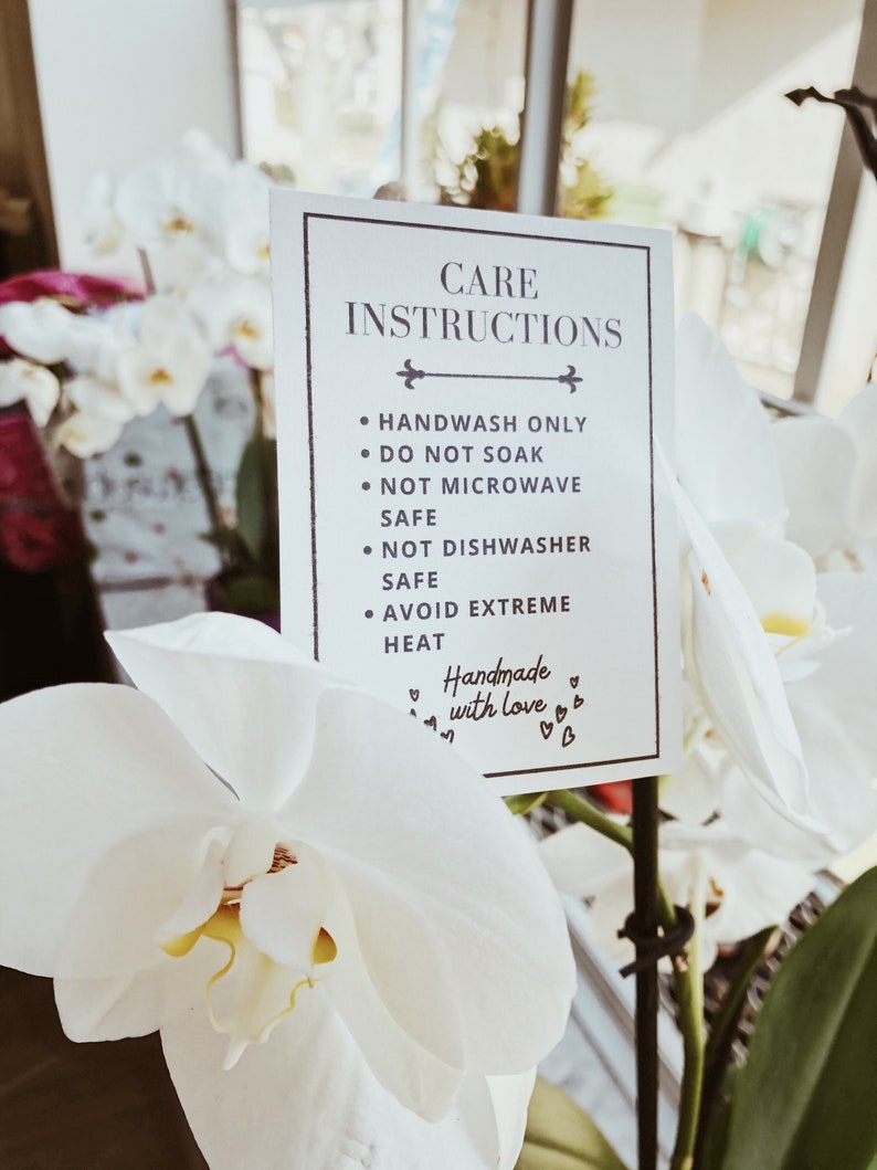 May include: A rectangular white card with a thin black border featuring the text CARE INSTRUCTIONS followed by bullet points: HANDWASH ONLY, DO NOT SOAK, NOT MICROWAVE SAFE, NOT DISHWASHER SAFE, AVOID EXTREME HEAT, and the phrase Handmade with love.