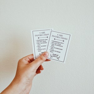 May include: Two rectangular white cards with black text reading CARE INSTRUCTIONS, followed by bullet points: HANDWASH ONLY, DO NOT SOAK, NOT MICROWAVE SAFE, NOT DISHWASHER SAFE, AVOID EXTREME HEAT, and the phrase Handmade with love with small hearts.