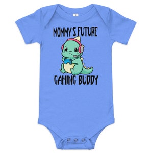 May include: Light blue baby bodysuit with a green dinosaur wearing headphones and holding a video game controller. The text "Mommy's Future Gaming Buddy" is printed on the bodysuit.