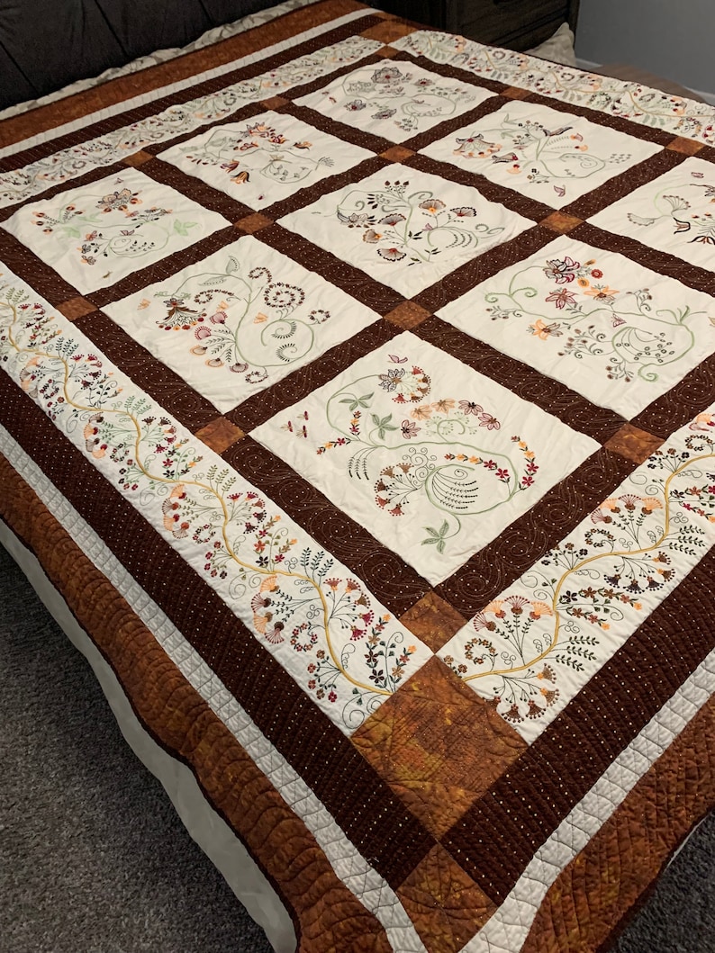 Puede incluir: Una colcha marr&oacute;n y blanca con un patr&oacute;n floral. La colcha est&aacute; hecha de cuadrados con un borde marr&oacute;n. La colcha est&aacute; en una cama.