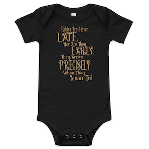 May include: Black baby onesie with gold text that reads "Babies Are Never LATE. Nor Are They EARLY. They Arrive PRECISELY When They Mean To!"