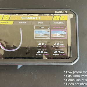 May include: A Garmin GPS device with a black case and a screen displaying a track map with data for Segment 3, including segment time, exit speed, turn entry, and minimum speed. The text "SEGMENT 3" is displayed at the top of the screen. The device is mounted on a surface with a low profile mount.