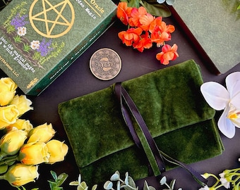 Può includere: Una pochette in velluto verde con chiusura a nastro nero, una moneta d'oro con la scritta "YES" incisa su di essa e un mazzo di tarocchi verde e oro con un pentagramma sulla copertina. Il mazzo è intitolato "Grimoire Oracle: Erboristeria e Magia del Giardino".