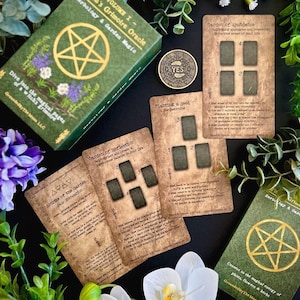 May include: A green box set with gold lettering and a pentagram design, titled "Herbology & Garden Magic." The set includes oracle cards with text and illustrations, a coin with "YES" on it, and is surrounded by greenery and flowers.