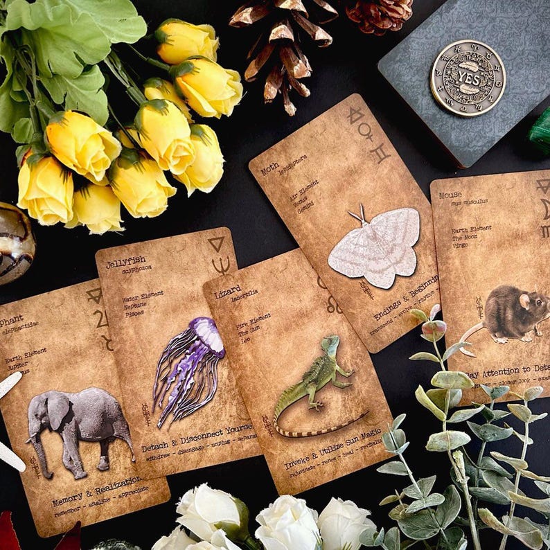 May include: A collection of tarot cards with animal illustrations, including an elephant, jellyfish, lizard, moth, and mouse. The cards are arranged with yellow roses, a coin that says "YES", and other decorative elements.