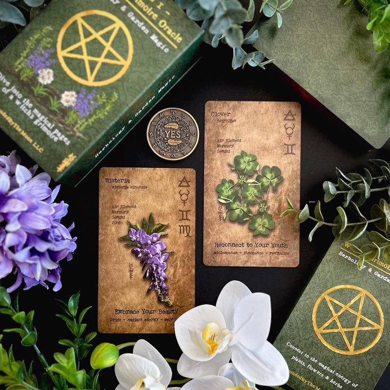 May include: An overhead shot of a green box set, oracle cards, and a coin with the word "YES". The cards feature botanical illustrations of wisteria and clover. The box set reads "Herbology & Garden Magic".
