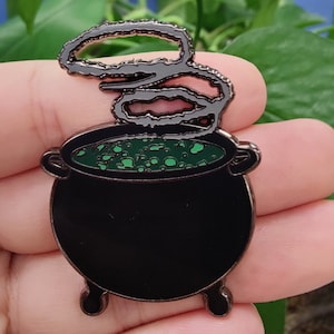 May include: A black cauldron with green bubbling liquid and a silver swirl of smoke rising from the top.