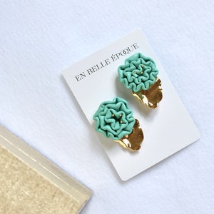 May include: A pair of green flower-shaped earrings with gold accents on a white card with the text "En Belle Époque".