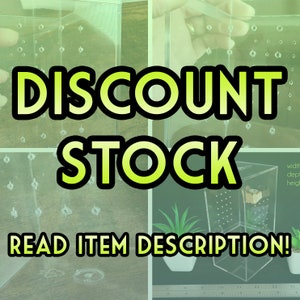 以下が含まれることがあります： 小さな穴のグリッドが付いた透明なアクリルボックス。ボックスには、「DISCOUNT STOCK」と「READ ITEM DESCRIPTION!」という緑と黒のテキストが書かれています。ボックスは定規の上に置かれています。