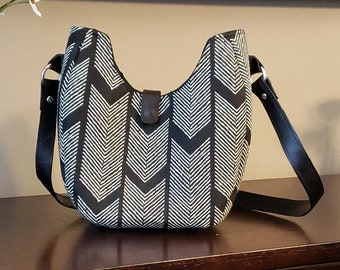 May include: A black and white chevron patterned crossbody bag with a black leather strap.