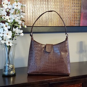 May include: A brown crocodile-embossed leather handbag with a single top handle and a flap closure.