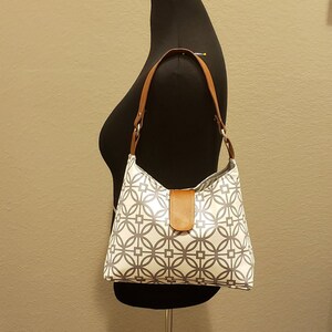 May include: A white and gray geometric patterned handbag with a brown leather strap and handle.