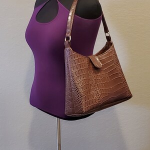 May include: A brown crocodile-embossed handbag with a shoulder strap on a black mannequin.