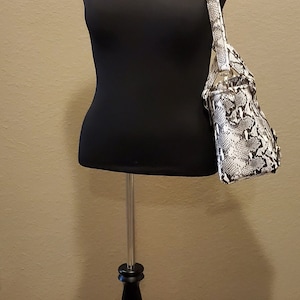May include: A black dress form with a white and black snakeskin handbag on a black tripod stand.