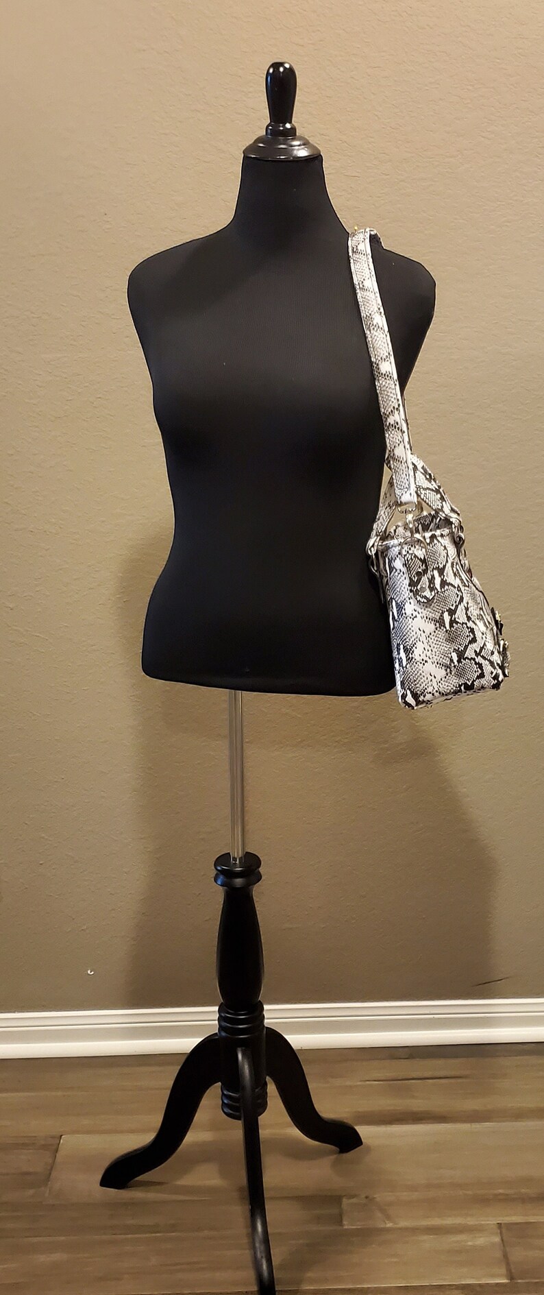 May include: A black dress form with a white and black snakeskin handbag on a black tripod stand.