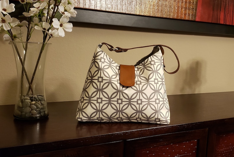 May include: A white and gray geometric patterned tote bag with a brown leather strap and flap.